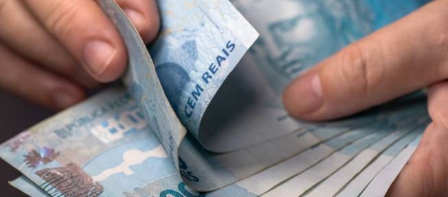 Várias notas de cem nas mãos de um homem