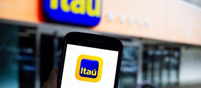Aplicativo do Itaú em primeiro plano; no segundo plano uma agência do banco