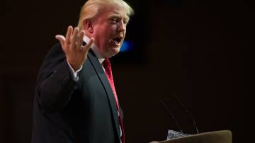 Presidente dos Estados Unidos, Donald Trump, com fundo preto, gesticulando durante comício
