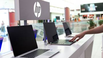 Bancada com diversos notebooks da HP, com o logo da companhia atrás