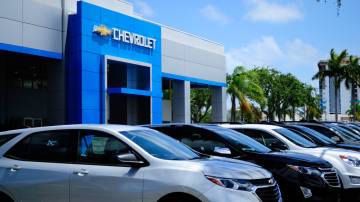 Concessionária da Chevrolet com a fachada azul e vários carros estacionados na frente da loja