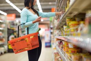 Mulher segurando cesta de supermercado enquanto escolhe alguns itens da prateleira
