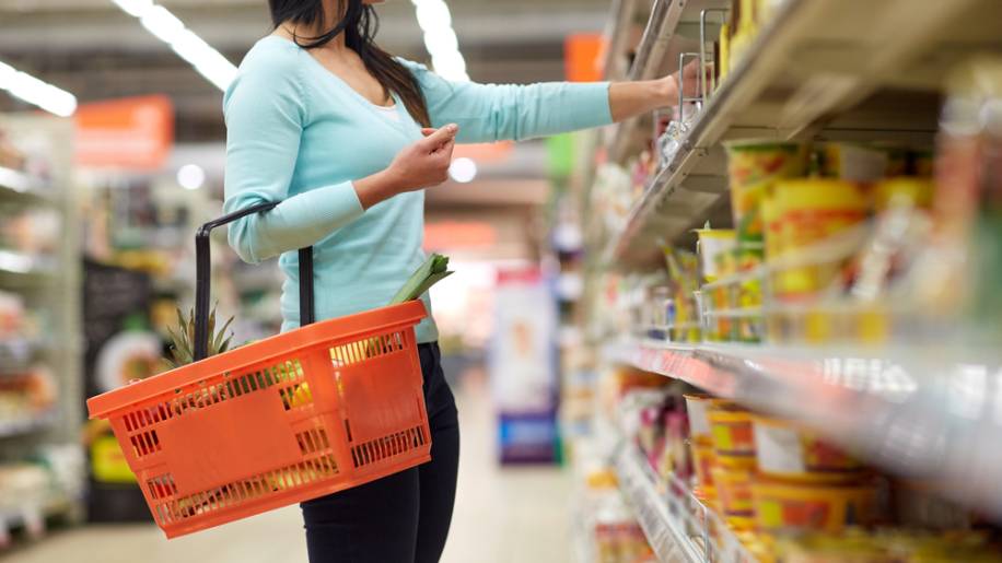 Mulher segurando cesta de supermercado enquanto escolhe alguns itens da prateleira