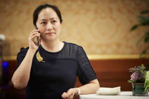 Meng Wanzhou, CFO da Huawei falando ao telefone em uma mesa de jantar. Ela usa um vestido preto e fala ao celular com a mão direita