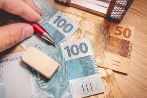 Real - Brazilian Currency. Money bills on a wooden table and a man holding a pen.