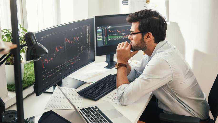 Successful traders. Back view of bearded stock market broker in eyeglasses analyzing data and graphs on multiple computer screens while sitting in modern office. Master Trader