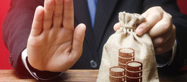 Crédito negado, homem faz sinal de negativo com uma mão enquanto segura saco de dinheiro com a outra, problemas financeiros, falta de dinheiro