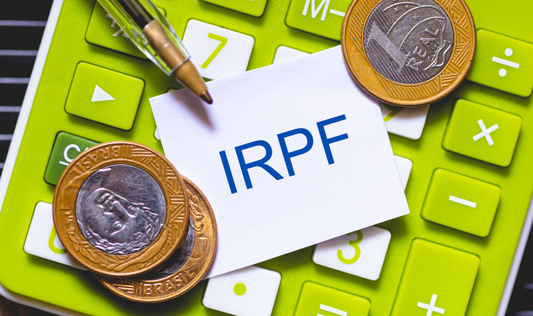 Foto de stock de As iniciais IRPF escritas na cor azul em um pequeno pedaço de papel. Caneta e Calculadora em composição. Economia brasileira, imposto de renda.