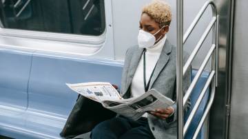 Mulher lê as notícias da semana no jornal em papel dentro do metrô