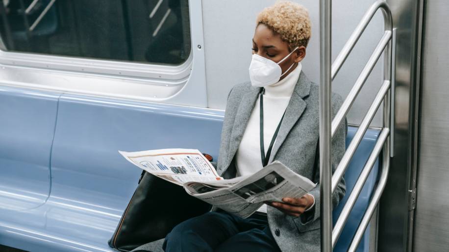Mulher lê as notícias da semana no jornal em papel dentro do metrô