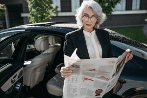 Mulher lê as notícias da semana em papel em frente a um carro