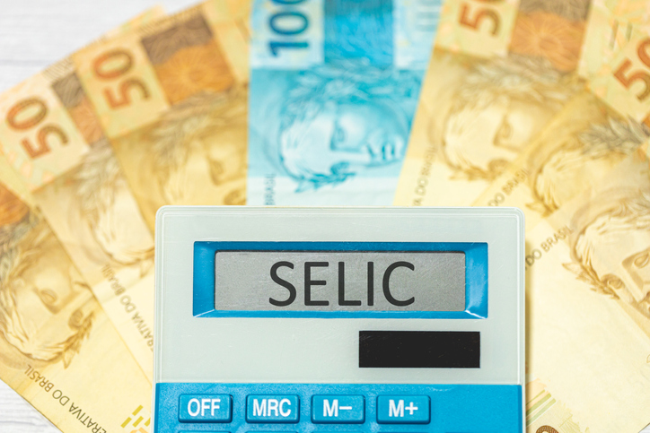 Foto de stock de As iniciais SELIC referem-se à taxa básica de juros no Brasil escritas na exibição de uma calculadora com notas de reais na composição. Economia e investimentos brasileiros.