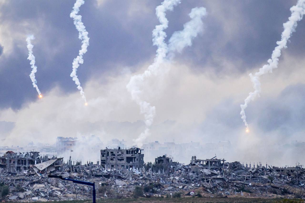 Esta foto tirada do sul de Israel, perto da fronteira com a Faixa de Gaza, mostra fumaça subindo após um ataque israelense, enquanto sinalizadores também são lançados sobre o norte de Gaza em 22 de novembro de 2023, em meio às batalhas contínuas entre Israel e o movimento palestino Hamas. Fotógrafo: John Macdougall/AFP/Getty Images