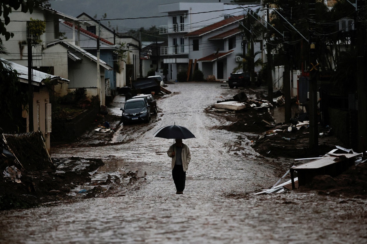 Um homem com guarda-chuva caminha por uma rua parcialmente destruída após enchentes em Mucum, Rio Grande do Sul, Brasil, 11 de maio de 2024. REUTERS/Adriano Machado