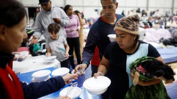 Refugiados venezuelanos Carina Gonzales e Xavier Velasquez recebem comida de um voluntário em abrigo em Porto Alegre depois que a casa onde viviam foi destruída pelas enchentes no estado (REUTERS/Adriano Machado)