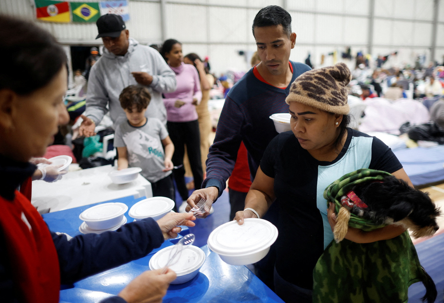 Refugiados venezuelanos Carina Gonzales e Xavier Velasquez recebem comida de um voluntário em abrigo em Porto Alegre depois que a casa onde viviam foi destruída pelas enchentes no estado (REUTERS/Adriano Machado)