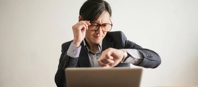 Homem olhando para o relógio em frente a um computador