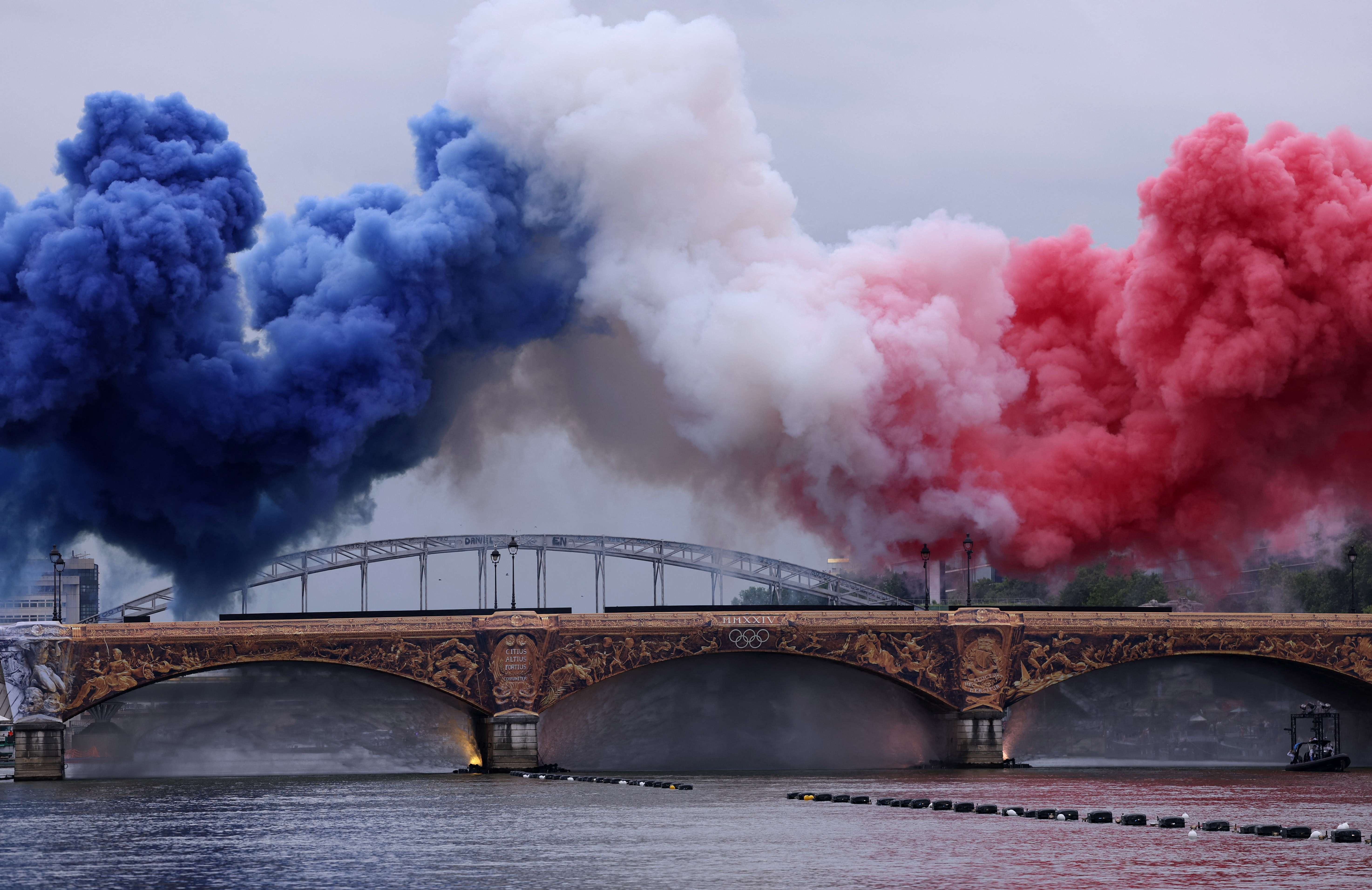 Nuvens de fumaça nas cores da bandeira da França são vistas acima da Pont d'Austerlitz durante a cerimônia de abertura 26/97/2024 (Foto: Amanda Perobelli)