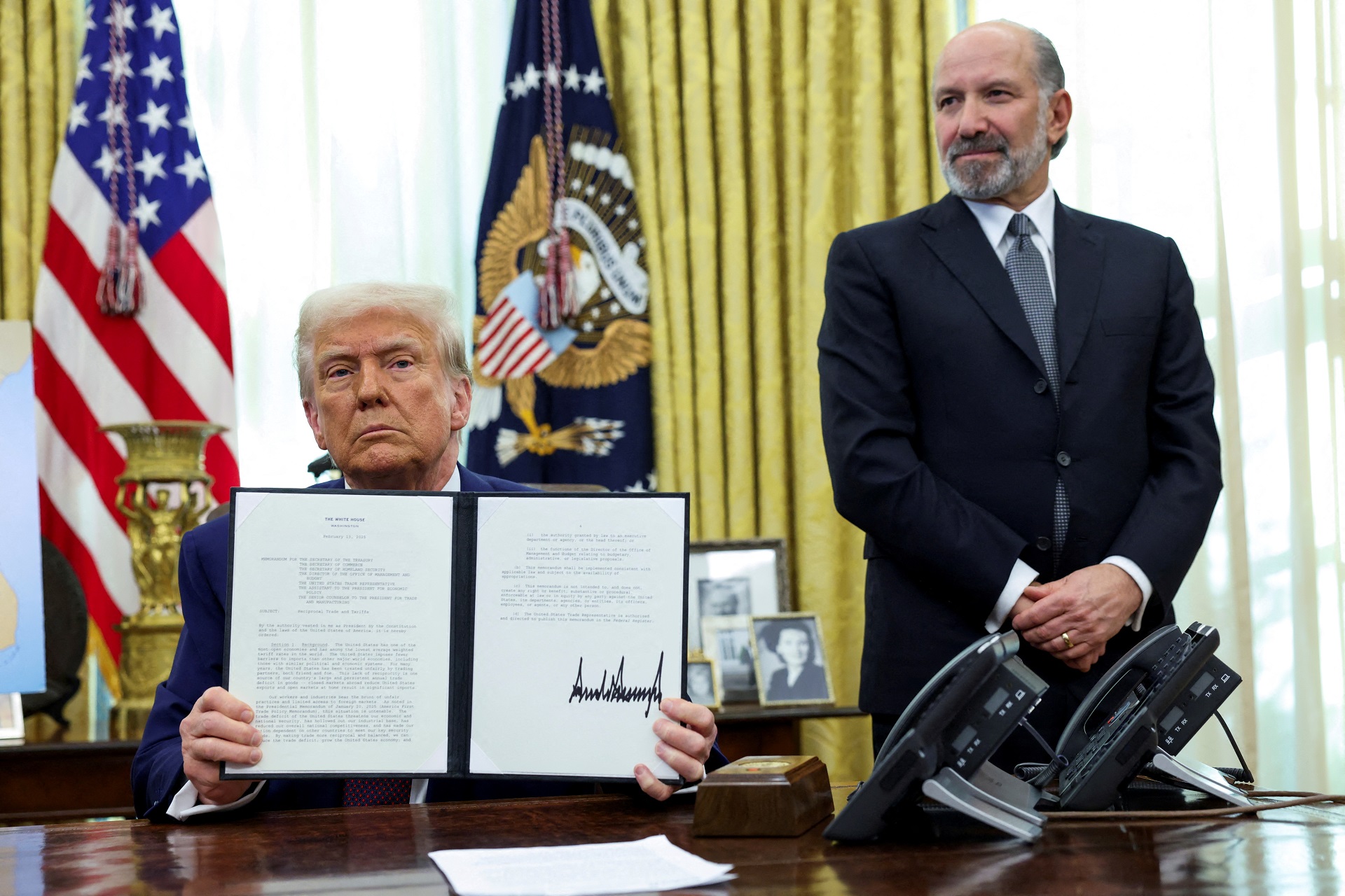 O presidente dos EUA, Donald Trump, segura uma ordem executiva sobre o aumento de tarifas, ladeado pelo secretário de Comércio dos EUA, Howard Lutnick, no Salão Oval da Casa Branca em Washington, D.C., EUA, 13 de fevereiro de 2025. REUTERS/Kevin Lamarque