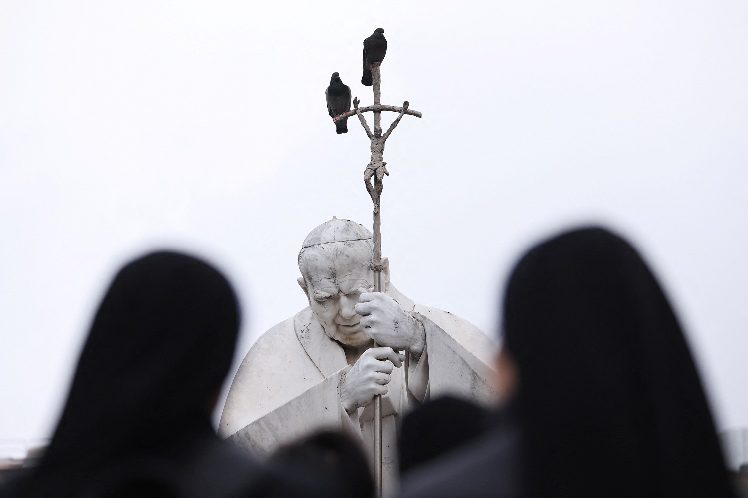 Estátua do falecido papa João Paulo 2º com pessoas rezando do lado de fora do Hospital Gemelli, onde o papa Francisco está internado em Roma
 25/2/2025     REUTERS/Claudia Greco
