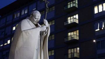 Uma estátua do falecido Papa João Paulo II está cercada por velas e flores do lado de fora do Hospital Gemelli, onde o Papa Francisco foi para continuar o tratamento de bronquite crônica, em Roma, Itália, em 17 de fevereiro de 2025. REUTERS/Guglielmo Mangiapane