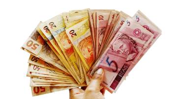Mão segurando cédulas de cinco, vinte e cinquenta reais em forma de leque