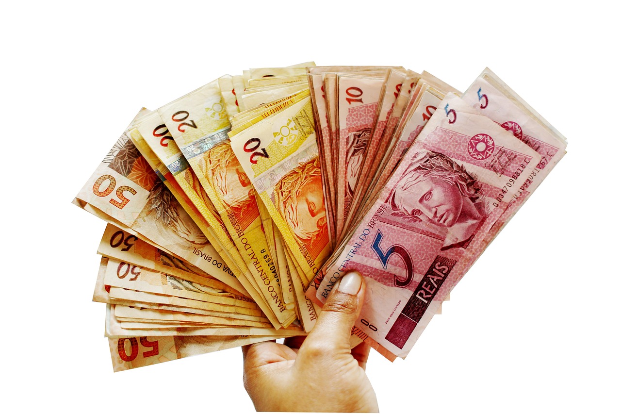 Mão segurando cédulas de cinco, vinte e cinquenta reais em forma de leque