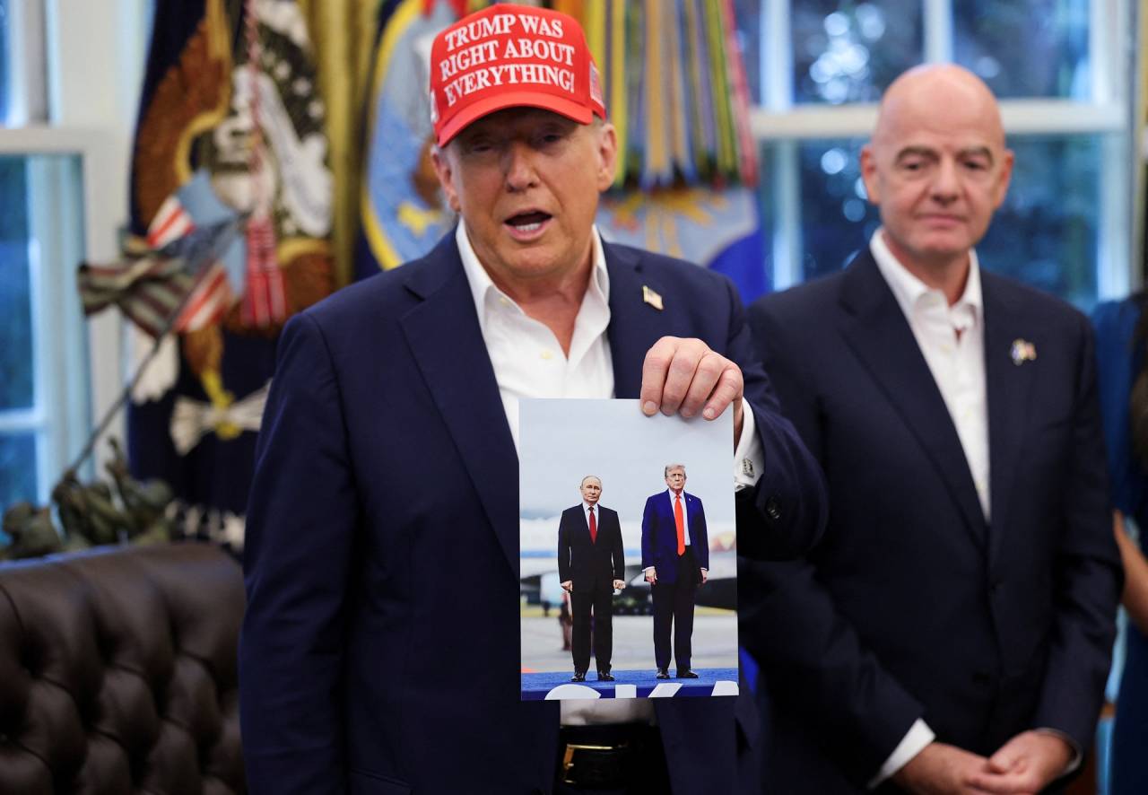 O presidente dos EUA, Donald Trump, segura uma imagem dele e do presidente russo, Vladimir Putin, de seu encontro no Alasca, enquanto o presidente da FIFA, Gianni Infantino, se levanta, enquanto o presidente Trump faz um anúncio sobre a Copa do Mundo da FIFA de 2026, no Salão Oval da Casa Branca em Washington, D.C., EUA, em 22 de agosto de 2025. REUTERS/Jonathan Ernst