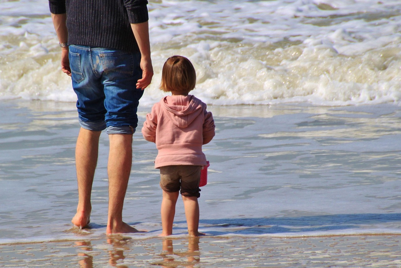 Pai e criança pequena de costas na beira do mar