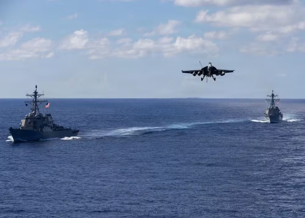 Jato F-18 se aproxima do porta-aviões USS Gerald Ford no Oceano Atlântico, com destróieres USS Mahan (à esquerda) e USS Bainbridge ao fundo em 13 de novembro de 2025. — Foto: Triniti Lersch/Marinha dos Estados Unidos