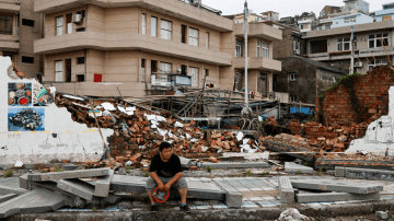 Uma pessoa senta-se ao lado de um muro desmoronado após a passagem do tufão Bavi na vila costeira de Dongsha, em Taizhou, província de Zhejiang, China, 12 de julho de 2026