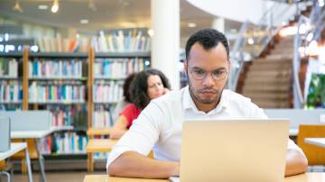 Estudante adulto masculino concentrado fazendo pesquisas na biblioteca